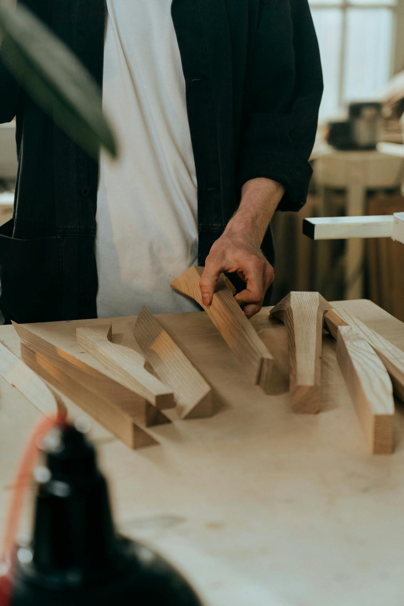 A craftsman choosing wooden pieces for a project in a sunlit workshop.